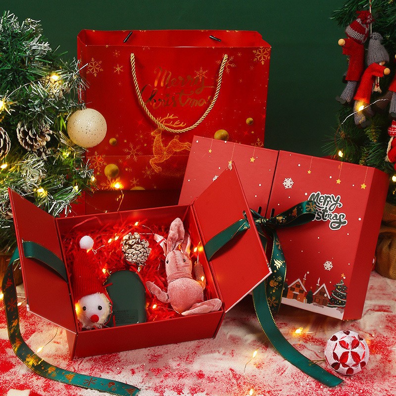 Christmas gift box with festive items including a plush toy, pinecone, and ornament, surrounded by lights. Nearby are a decorated tree, red gift bag, and holiday decorations.