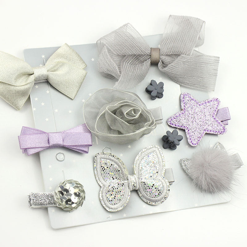 A variety of sparkly hair accessories on a white background. Includes bows, a flower, star, and butterfly, in shades of silver, gray, and purple with glitter and sequins.