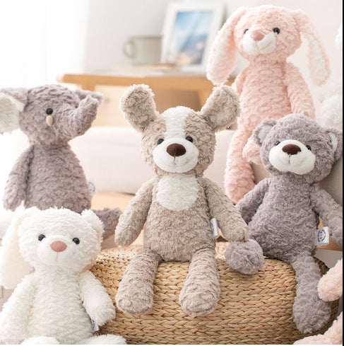 A group of plush toys sits on a woven basket and surrounding furniture. The toys include a dog, rabbit, bear, and elephant, all with soft, fluffy textures in pastel colors.