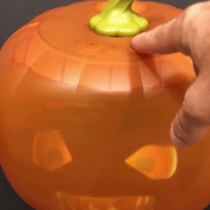 Plastic jack-o'-lantern with glowing eyes and carved face, featuring a green stem. A hand is pointing at the top of the pumpkin.