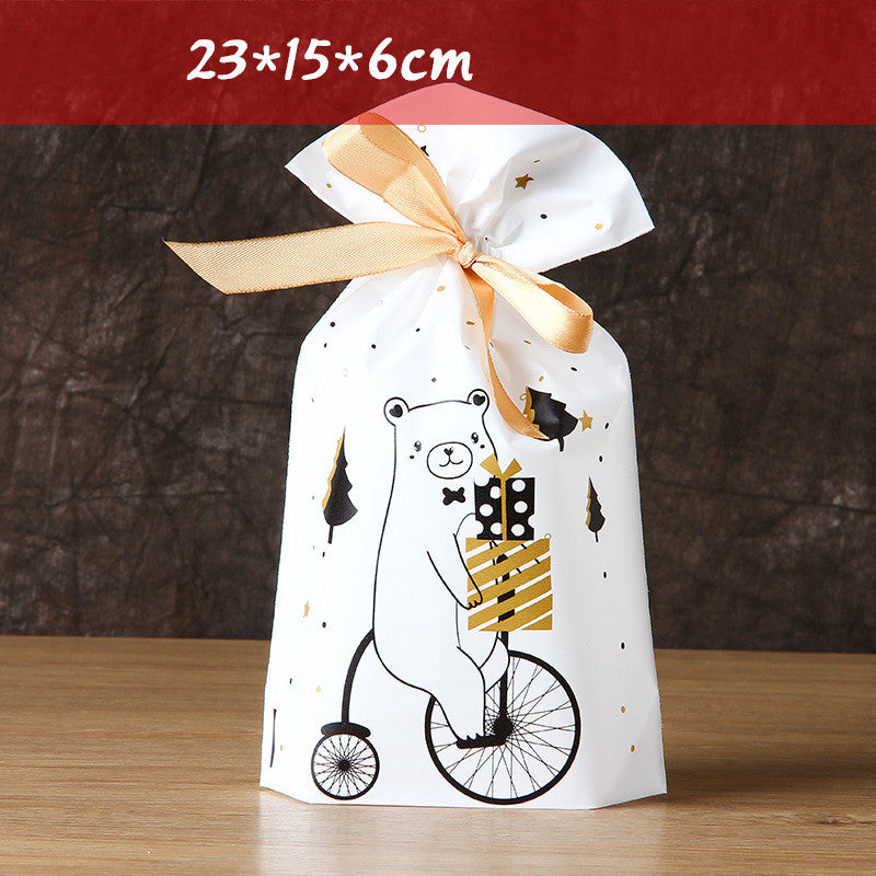 Decorative gift bag with a bear illustration riding a unicycle, holding presents. The bag is tied with a golden ribbon and measures 23x15x6 cm. Black and gold accents.