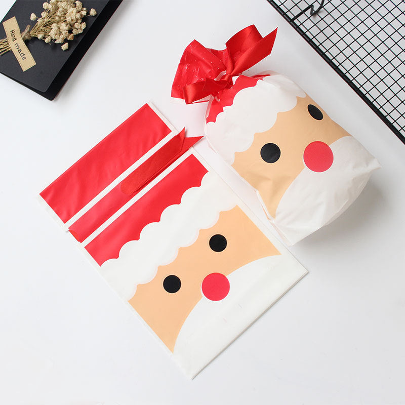 Festive Santa-themed gift bags with cartoon faces, one filled and tied with a red ribbon. Nearby, a black tray with dried flowers and a handmade label.