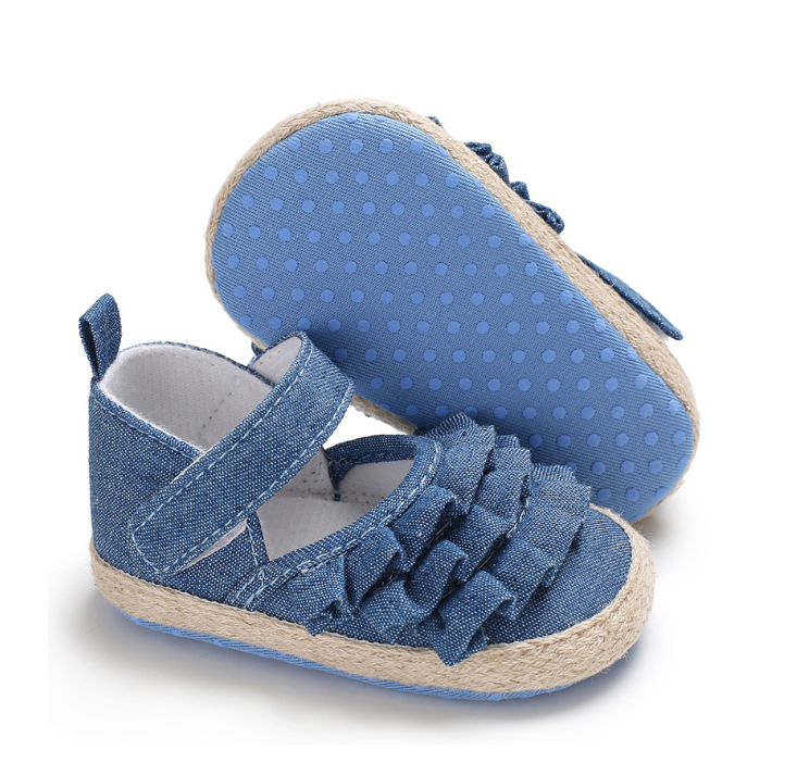 Blue baby shoes with textured soles, Velcro straps, and decorative ruffles on top. The outer material is denim-like, and the soles have a light blue dotted pattern.
