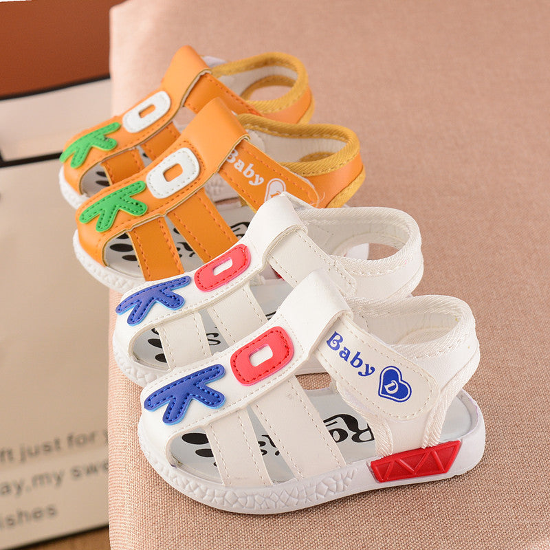 Two pairs of baby sandals on a surface; one pair is white with red and blue accents, the other is orange with green and white details. Both have the word "Baby" on them.