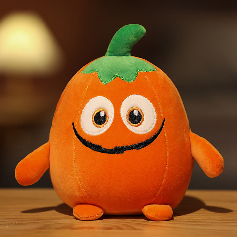 A plush toy shaped like an orange pumpkin with big round eyes, a smiling mouth, and a green stem on top, sits on a wooden surface against a blurred background.