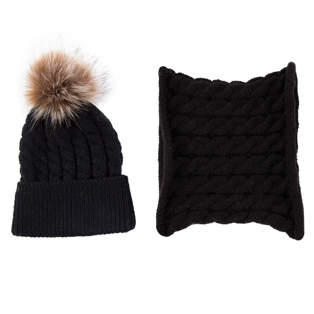 Black knit beanie with a brown faux fur pom-pom, alongside a matching black knit neck warmer, both featuring a braided pattern.