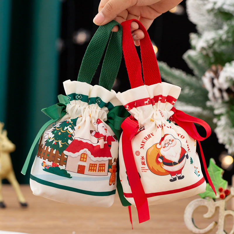 Two festive drawstring gift bags with Christmas-themed designs, including Santa and reindeer, are held in hand. One bag has green handles and the other red, near a snowy tree.