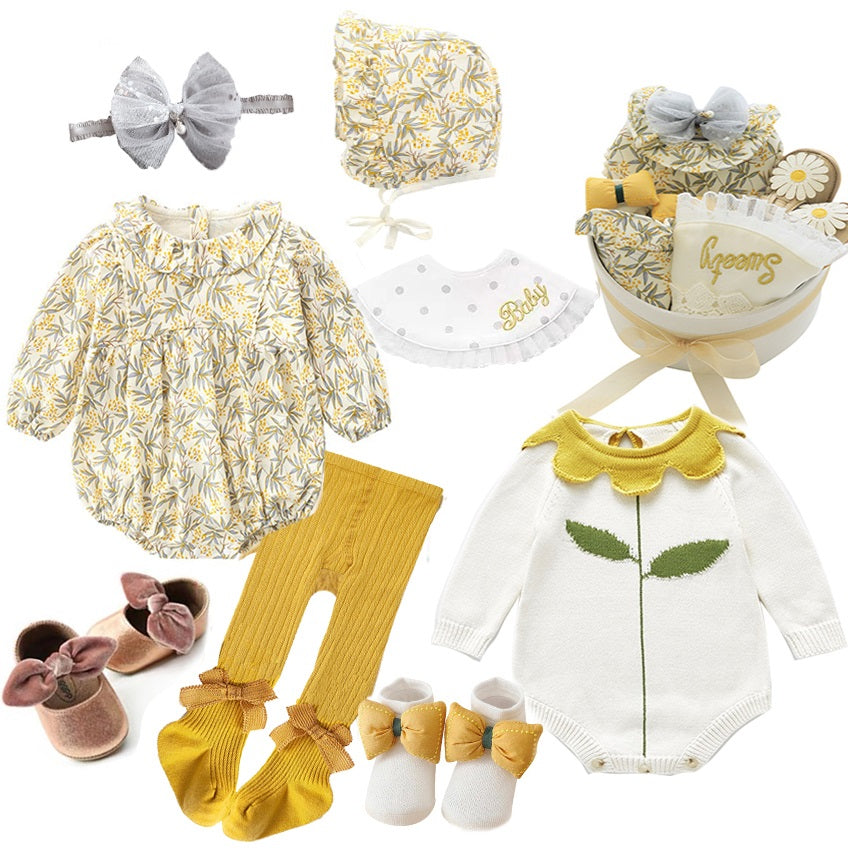 Baby gift set with floral romper, matching bonnet, yellow tights, white onesie with leaf design, bow headband, pink shoes, bib, and basket with a "Sweet" blanket.