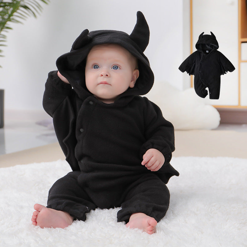 Baby in a cozy black onesie with horned hood sitting on a white rug. A small image of the outfit is shown in the background. Indoor setting with soft lighting.