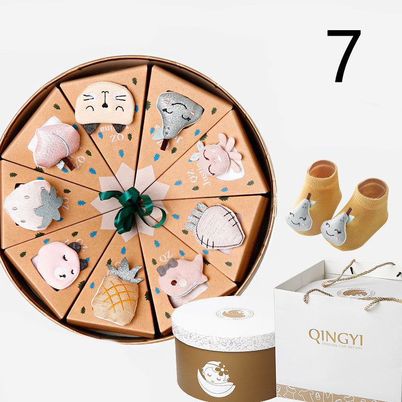 Round gift box with 12 triangle compartments, each with a cute animal decoration. Includes a pair of yellow baby socks with smiling pears, and a white gift bag labeled "QINGYI."