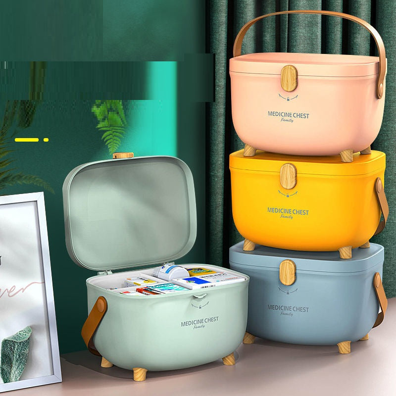 Stacked pastel-colored medicine chests with wooden knobs and handles; one open case reveals organized medical supplies. A framed picture and green curtains are in the background.