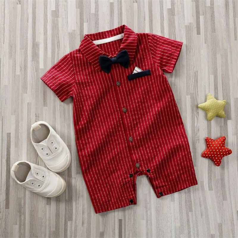 Red striped baby romper with a navy bowtie and pocket square, white slip-on shoes, and two plush star toys on a light wooden floor.