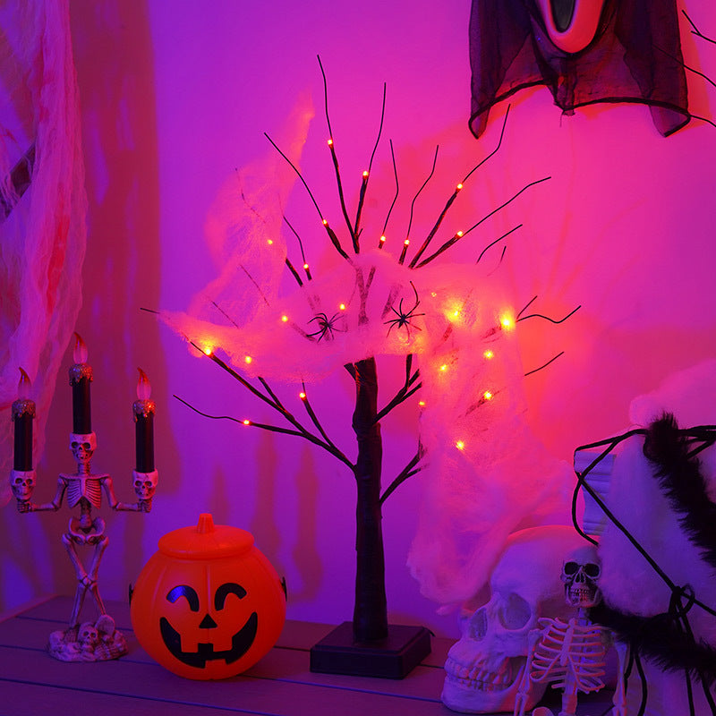 A spooky Halloween scene with a glowing branch tree wrapped in cobwebs and spiders, surrounded by a skull, skeleton, pumpkin bucket, and candle holder under purple lighting.