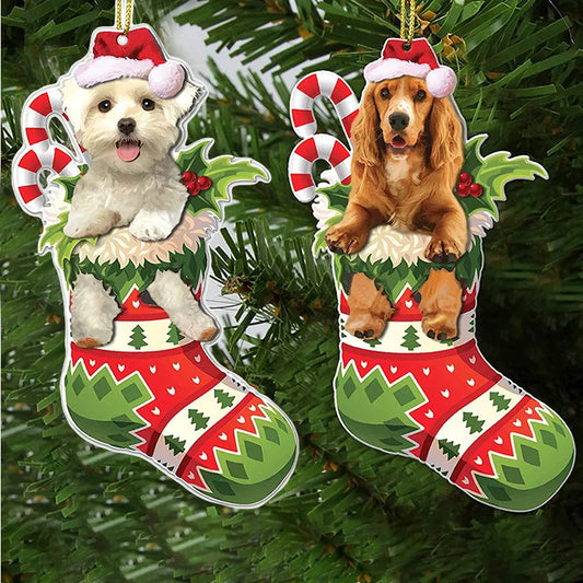 Two Christmas ornaments featuring dogs in festive stockings with candy canes and holly, hanging on a green Christmas tree. One dog is white, the other is brown.