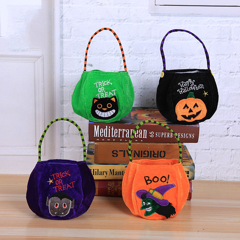 Four Halloween-themed bags with handles sit on a wooden surface. Designs include a black cat, jack-o'-lantern, vampire, and witch. Two bags say "Trick or Treat" and "Boo!".