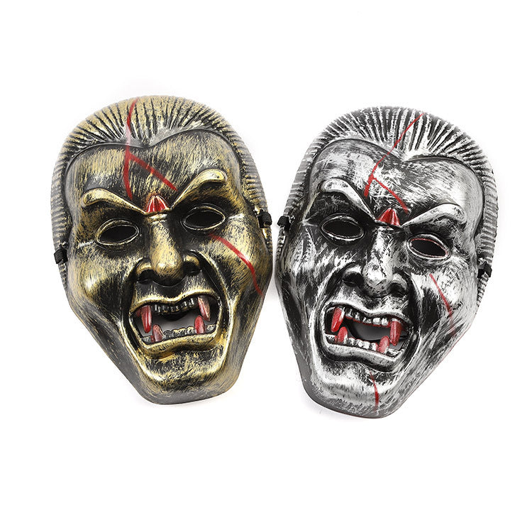 Two metallic vampire masks with exaggerated fangs and red scars. The left mask is gold and the right is silver. Both have an expression of anger or intimidation.