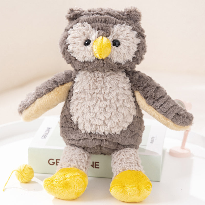 Fluffy stuffed owl toy with a gray and beige body, yellow feet, and beak, sitting on a book with a small yellow yarn ball nearby.