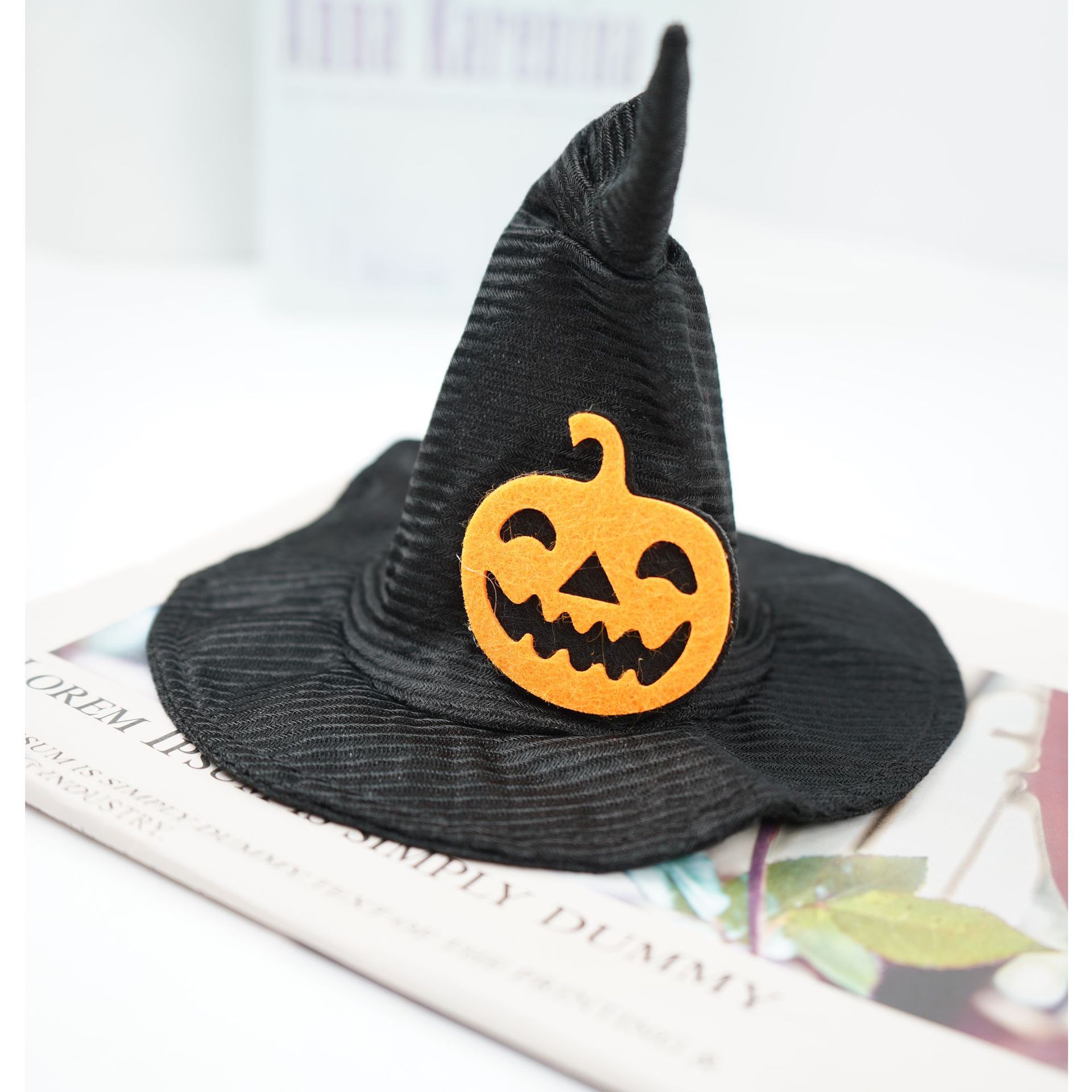 A black witch hat with a grinning orange pumpkin face decoration sits on an open book with blurred text and images.