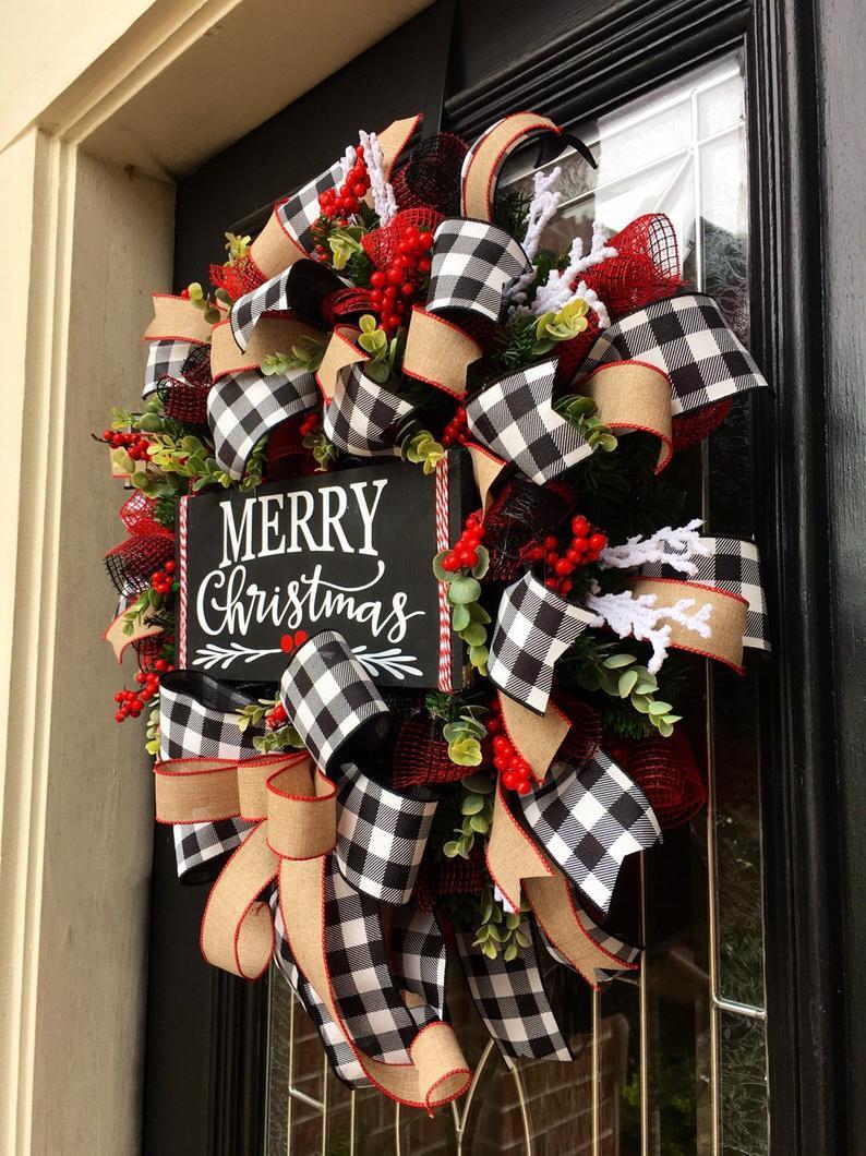 Festive wreath with plaid ribbons, red berries, and greenery, featuring a "Merry Christmas" sign, hangs on a door, evoking holiday cheer and warmth.