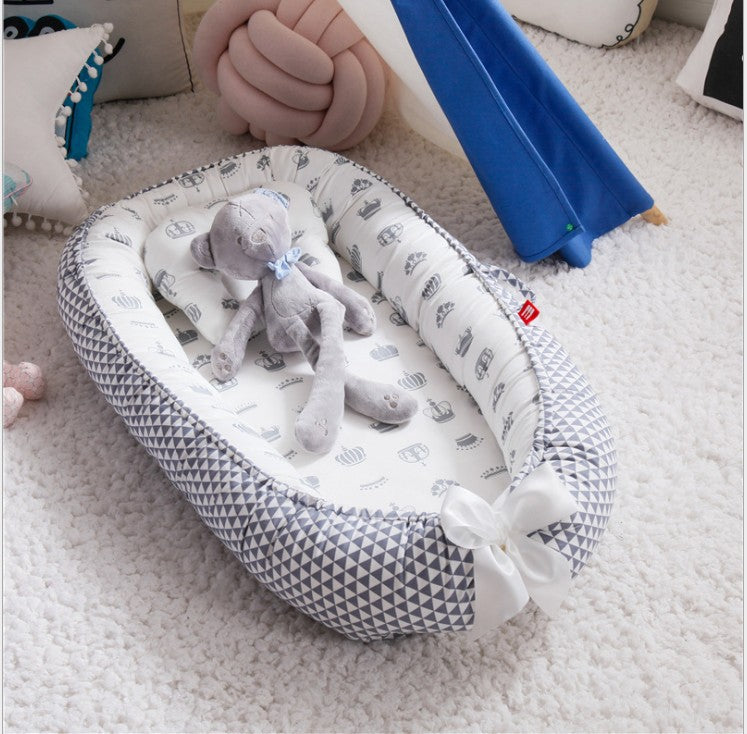 Cozy baby nest with geometric and animal print, placed on a soft carpet. A gray teddy bear with a blue bow sits inside, surrounded by decorative cushions.