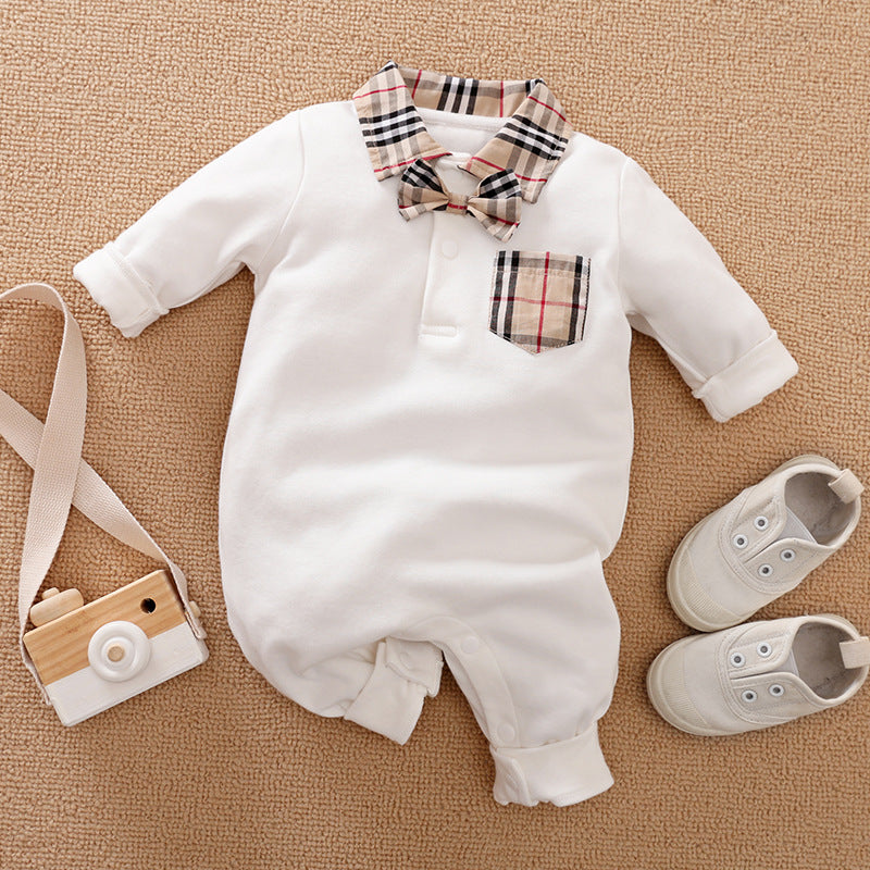 Baby outfit with a white romper featuring a plaid collar, pocket, and bow tie, paired with white sneakers and a wooden toy camera, laid out on a beige surface.