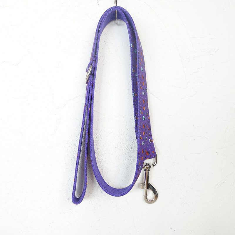 Purple dog leash with small colorful dots, featuring a metal clasp and an adjustable buckle, hanging on a hook against a plain white background.