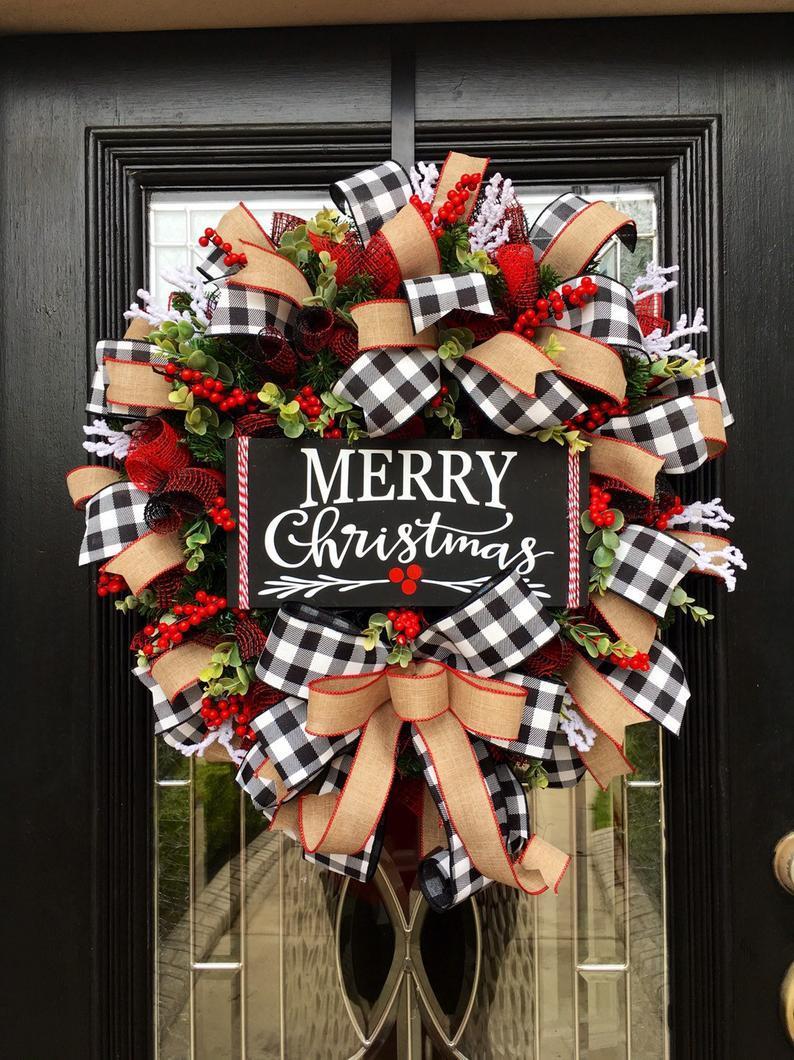 Festive Christmas wreath on a door with "Merry Christmas" sign, adorned with black-and-white checkered bows, red berries, green foliage, and burlap ribbons.