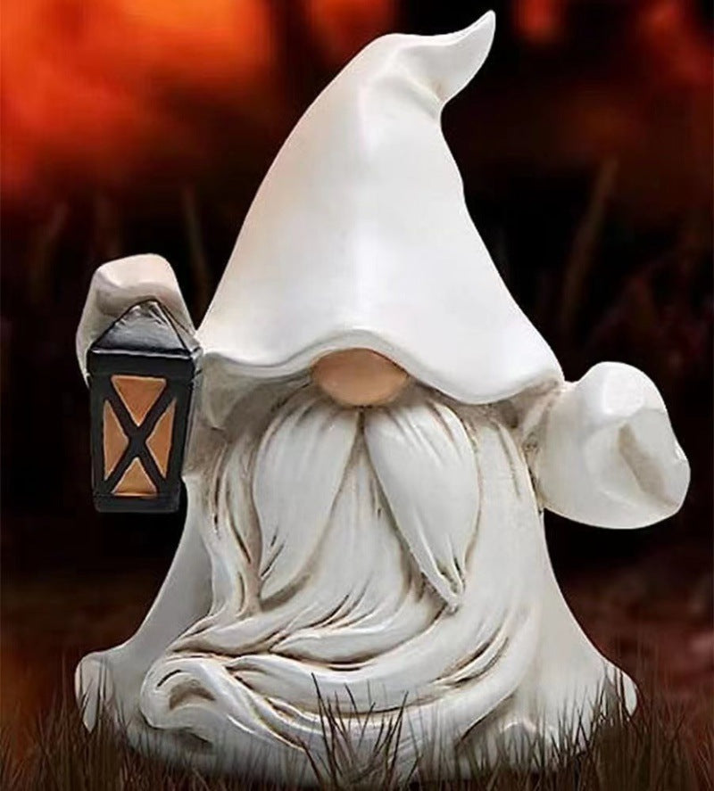 A gnome figurine with a tall, pointed white hat, long white beard, and holding a lantern stands on grass with a blurred, warm-toned background.