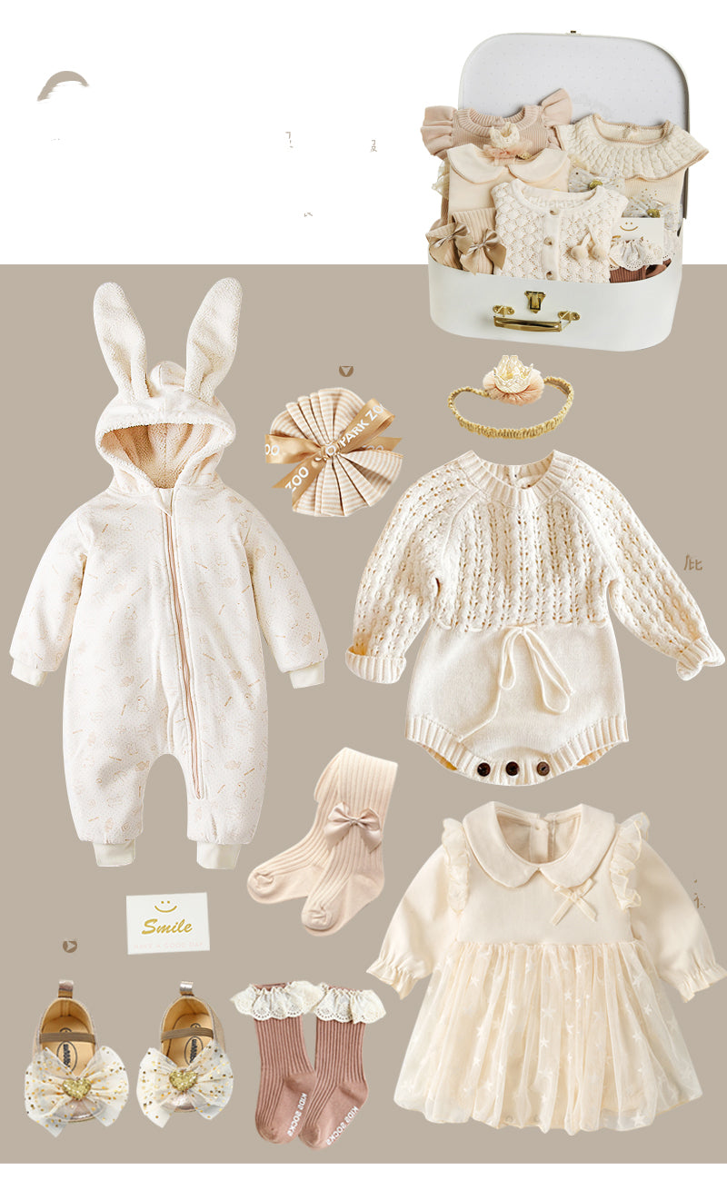 A collection of beige baby clothes including a bunny-eared onesie, knitted romper, dress, socks, shoes, and hair accessories, displayed with a suitcase and smiley card.