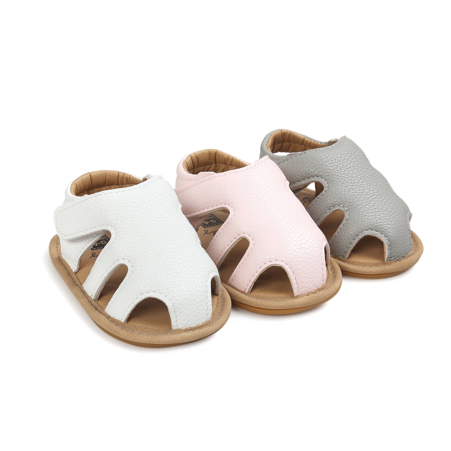 Three pairs of baby sandals in white, pink, and gray are arranged in a row. They have open toes and a textured surface with tan soles.