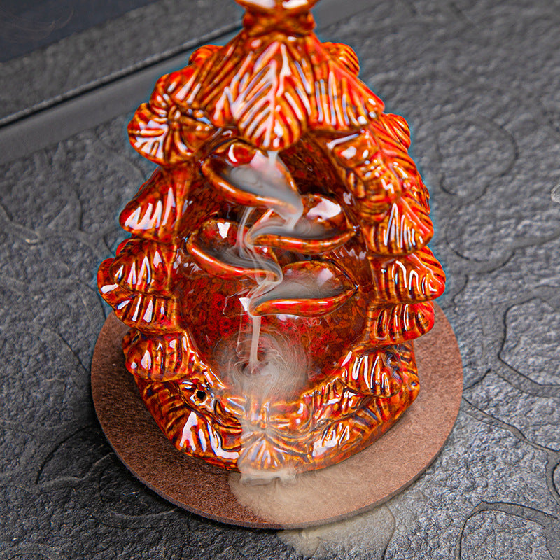 Intricately designed orange incense holder with leaf patterns, featuring cascading smoke flowing downwards, set on a textured dark surface.