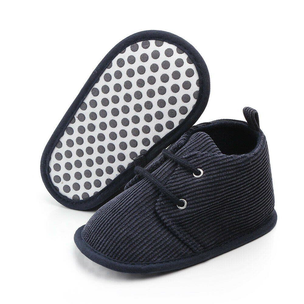 Dark blue corduroy baby shoe with laces, shown with one shoe's polka dot sole facing up and the other upright. Textured design, soft material, suitable for infants.