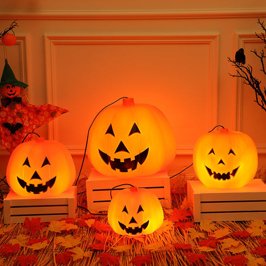 Four glowing jack-o'-lanterns with carved faces sit on white crates, surrounded by orange and red autumn leaves. A scarecrow and a branch complete the Halloween scene.