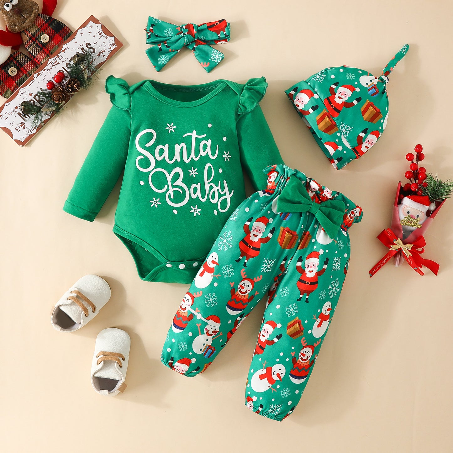Green baby outfit set with "Santa Baby" onesie, Santa-themed pants, hat, and bow. Includes white shoes and festive decorations with a Santa figure and gift wrap.