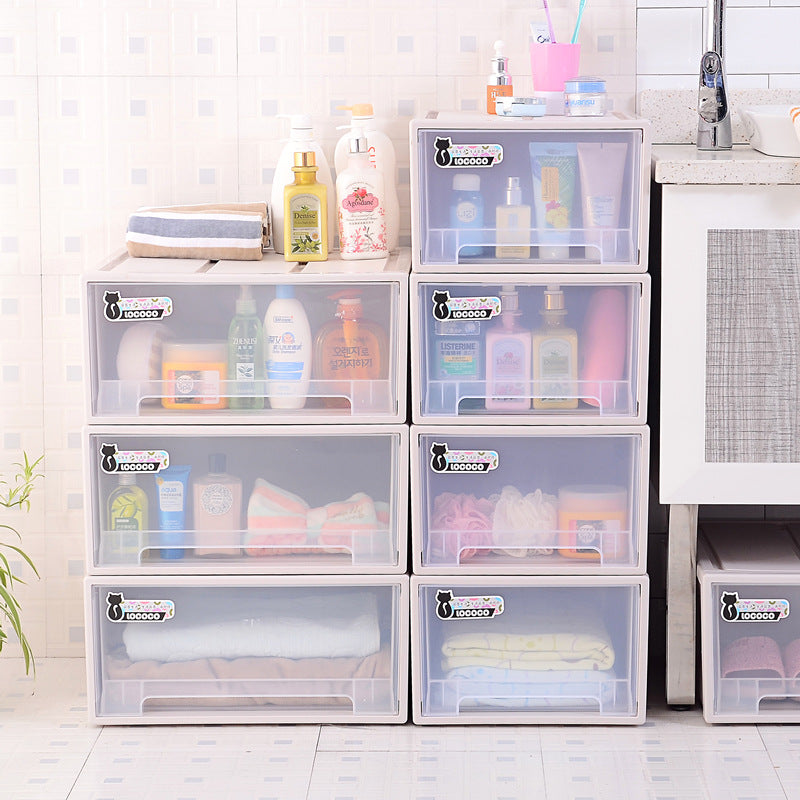 Plastic storage drawers filled with toiletries, towels, and clothes, organized beside a sink. Various bottles and a toiletry bag rest on top. White tiled wall in background.
