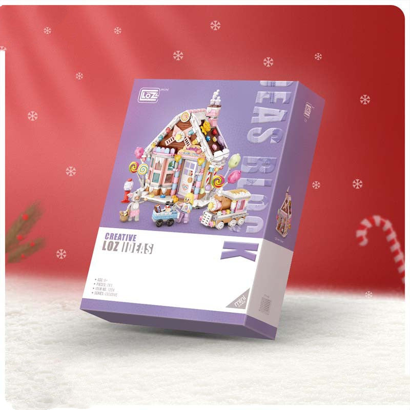 Box of a colorful gingerbread house building set with candy-themed decorations. The background is red with snowflakes and candy canes, creating a festive atmosphere.