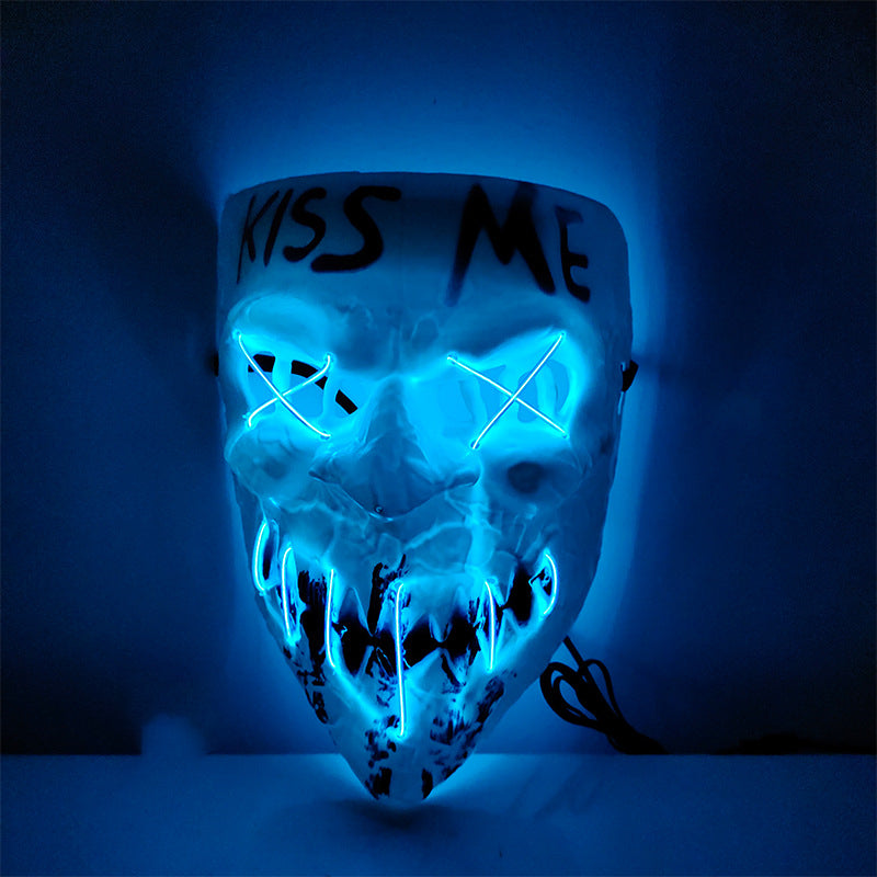 Glowing mask with blue neon light features "Kiss Me" text, jagged teeth, and crossed-out eyes, creating an eerie effect against a dark background.