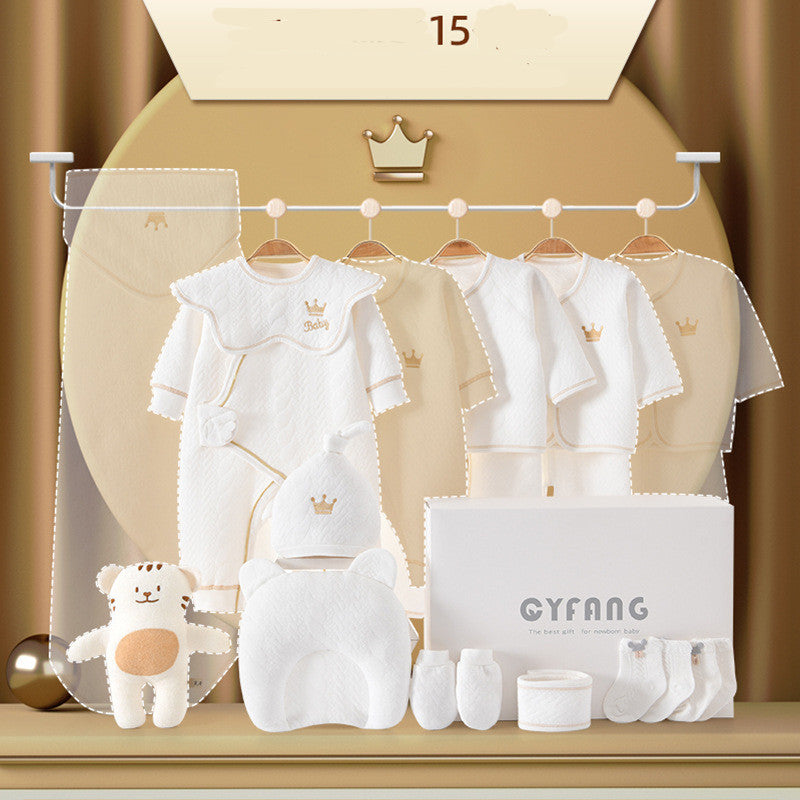 Baby clothing set featuring white outfits with crown motifs, a hat, plush toy, pillow, socks, mittens, and gift box, all arranged against a gold background.