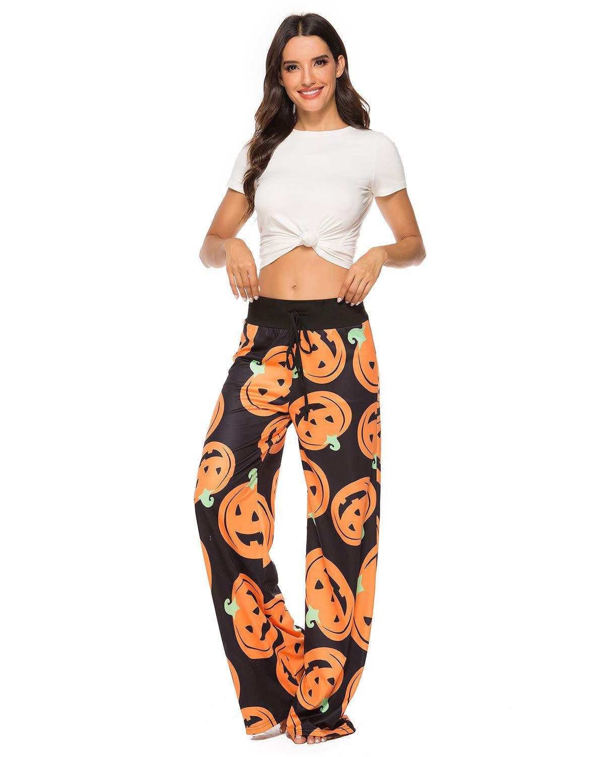 Woman in a white knotted t-shirt and black Halloween-themed pants with pumpkin patterns stands smiling against a white background.