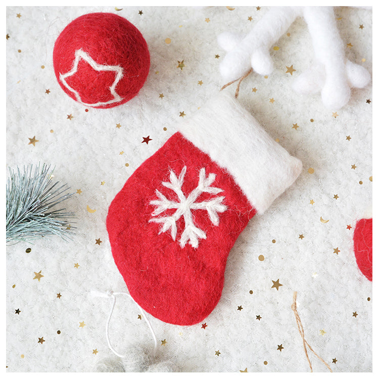 Red felt Christmas stocking with a white snowflake design, alongside a red ball with a star pattern. Background features gold stars and a sprig of blue pine.