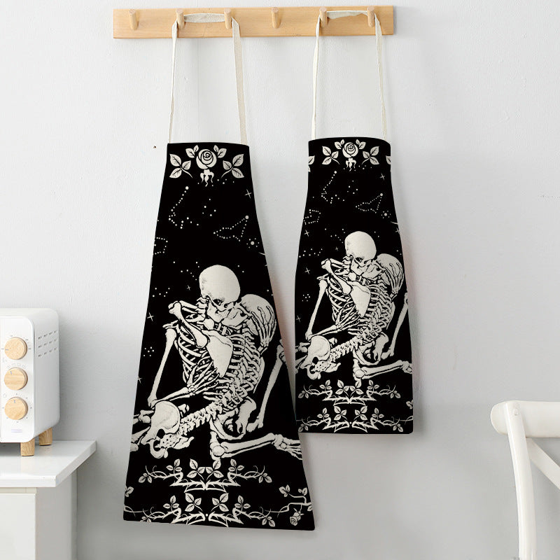 Two black aprons with white skeleton designs sit on a wooden rack. The skeletons are intertwined, surrounded by stars and roses, creating a whimsical, gothic style.