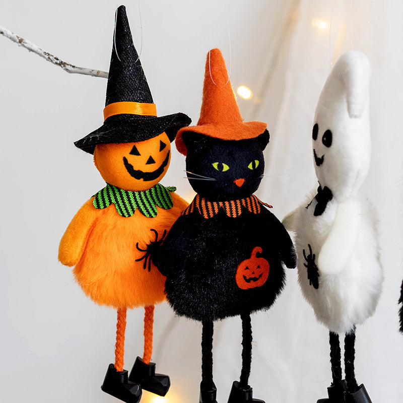 Three plush Halloween decorations—a pumpkin, black cat, and ghost—wearing witch hats and hanging on a branch. Each features festive details like spiders and pumpkins.