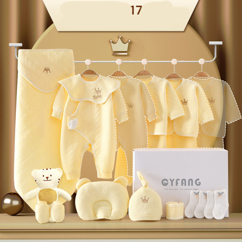 A collection of pastel yellow baby clothes and accessories, including onesies, socks, a plush bear, and a neck pillow, displayed on a rail with a decorative crown emblem.