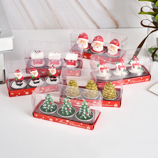 Festive Christmas-themed candle sets featuring snowmen, Santa Claus figures, golden pinecones, and decorated trees packaged in transparent boxes with red bases.