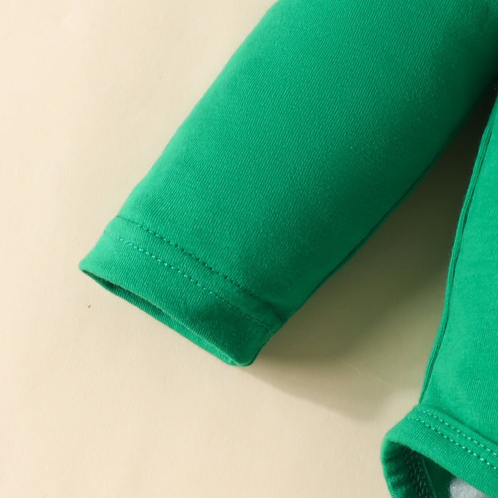 Close-up of a long-sleeve green shirt cuff on a cream background. The fabric appears soft, with visible stitching near the hem.