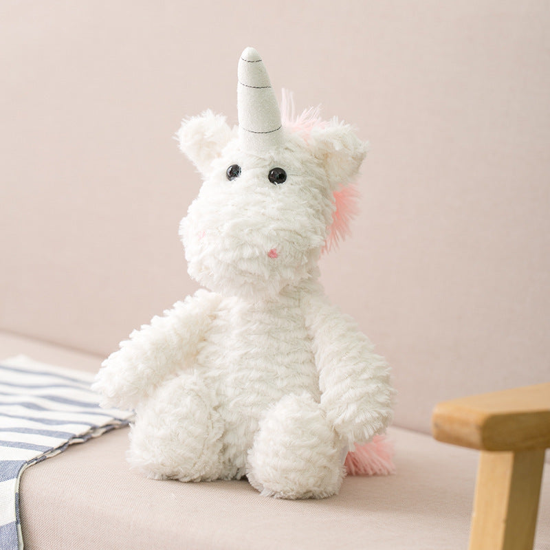 Fluffy white unicorn plush with a gray horn, black eyes, and pink mane sits on a light beige couch next to a striped cloth, creating a cozy and whimsical scene.