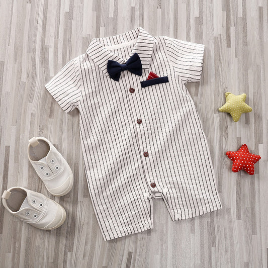 Striped baby romper with navy bow tie and red pocket square on a wooden floor, paired with white shoes. Two star-shaped toys, one green and one red, lie nearby.