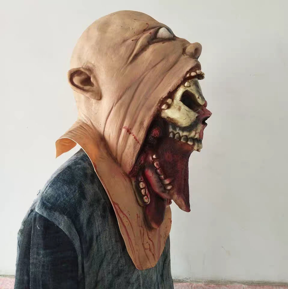 Side view of a person wearing a Halloween mask resembling a humanoid with grotesque features, including a wide, open mouth revealing a skull and exaggerated facial details.