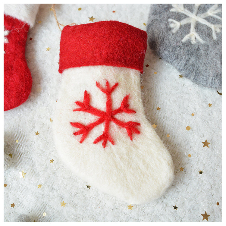 A felt Christmas stocking with a red snowflake design and red top, lain on a white textured surface adorned with gold star confetti.