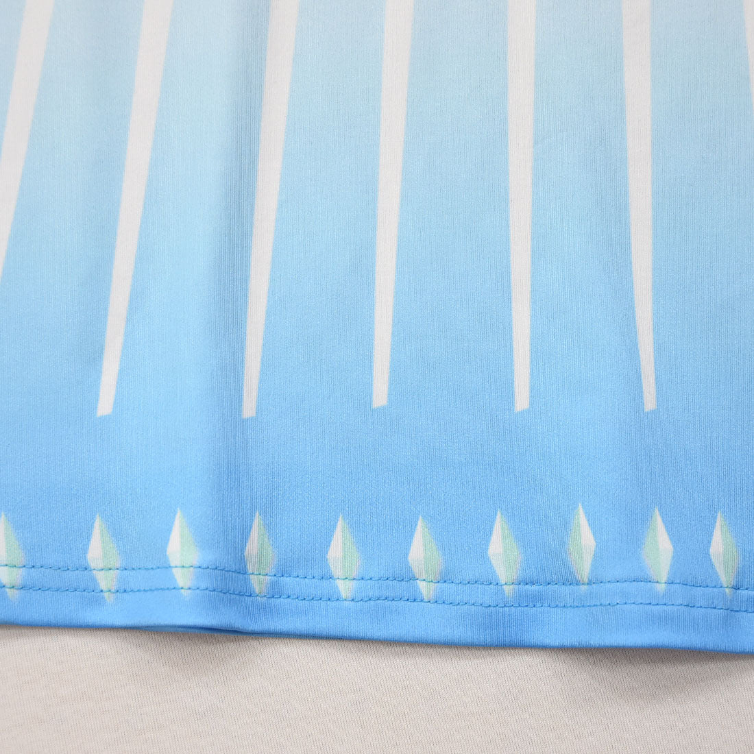 Close-up of a blue fabric with a design of long white vertical lines and small crystal-like shapes at the bottom edge.